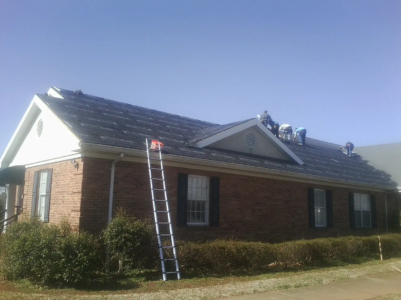 Crew tearing shingles off a brick ranch roof with a ladder set — Emergency Roof Repair work by our crew in Rock Hill