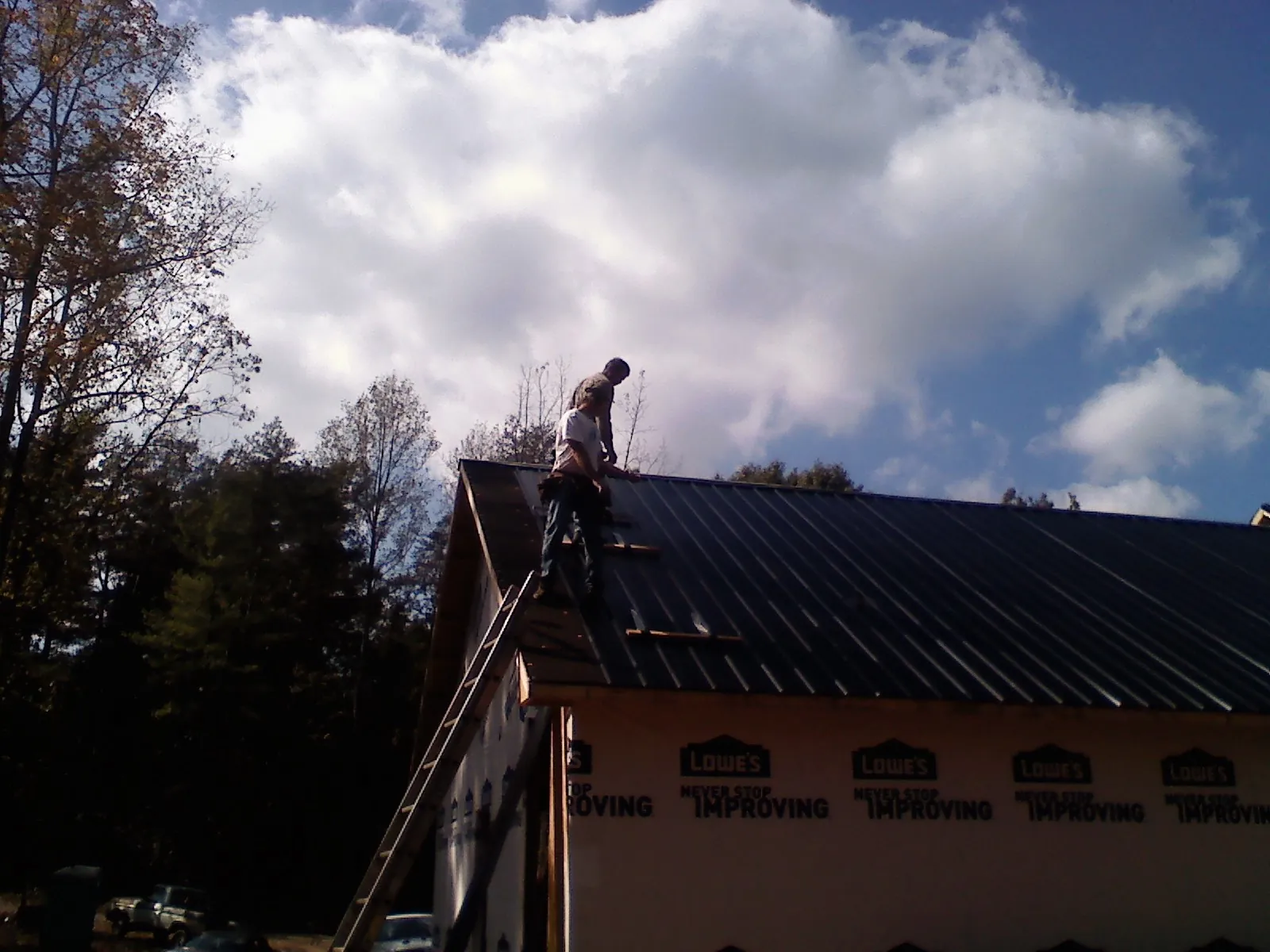 Roofer fastening dark metal panels high against a cloudy sky in Rock Hill