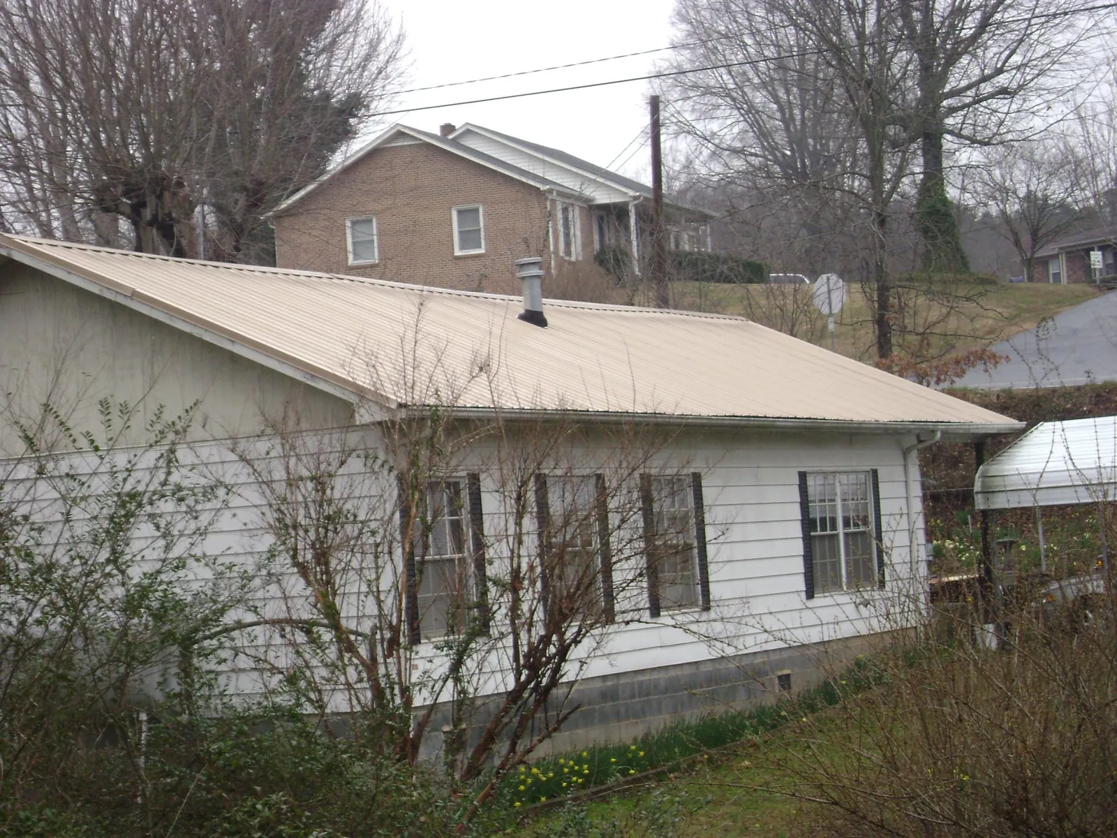 Tan metal roof on a white sided house set into a hillside — Commercial Roofing by Roofing Brothers in Rock Hill